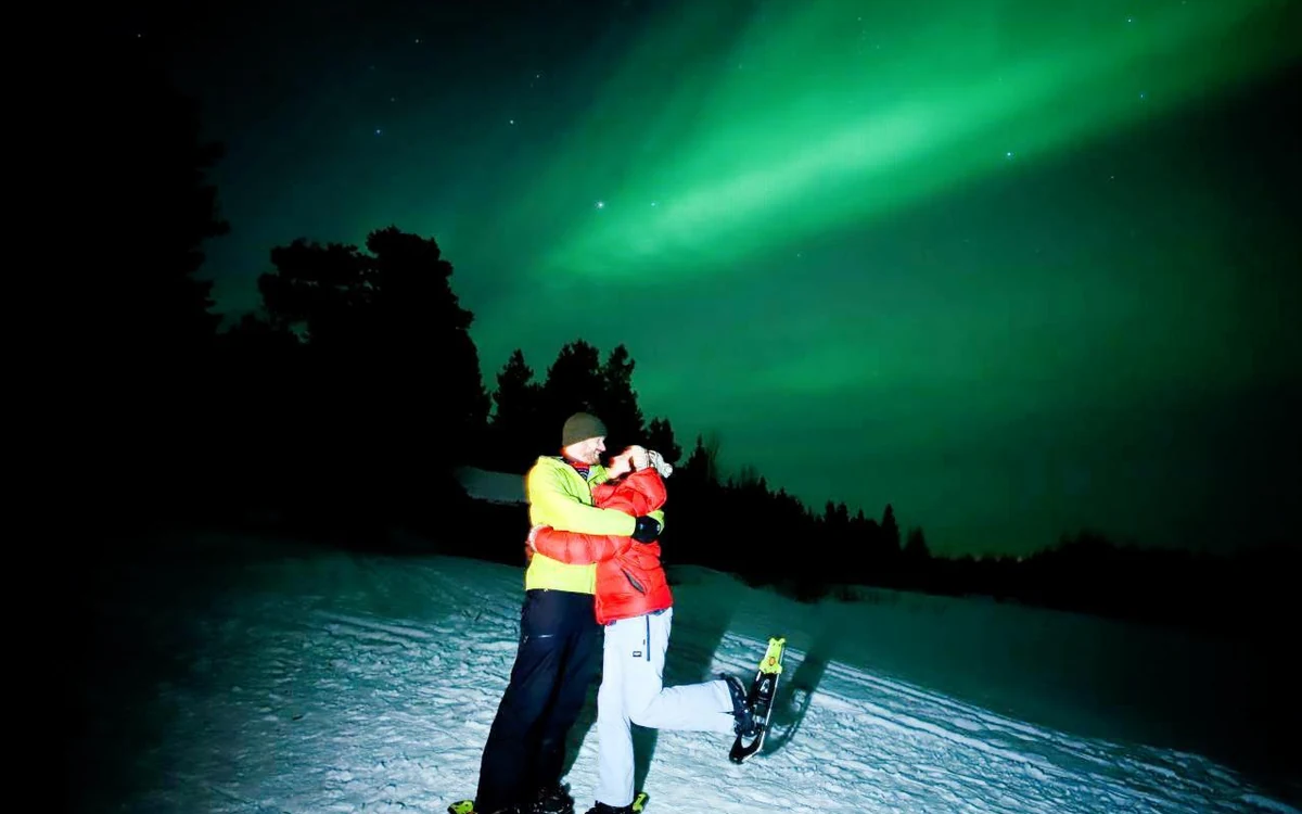 A camera on a tripod pointed at a dark starry sky over snow in Lapland