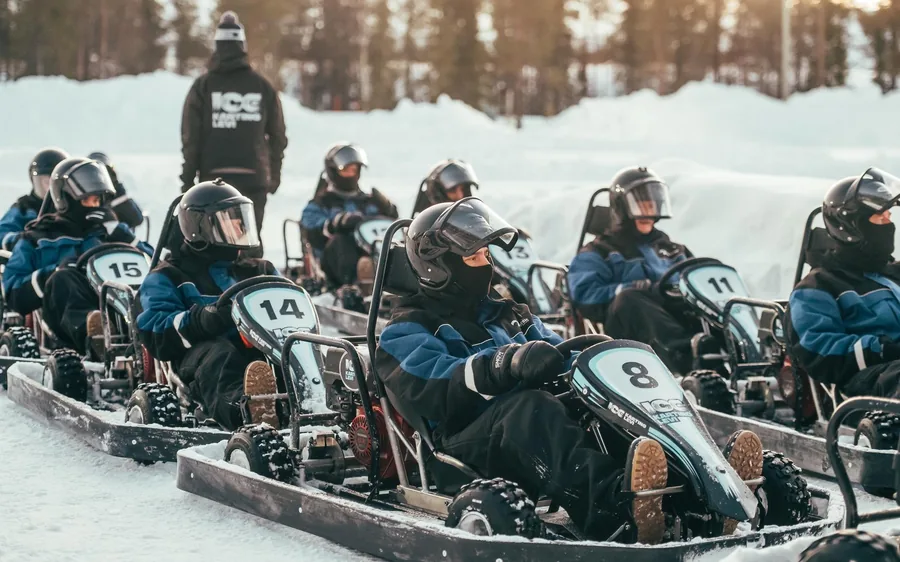 Rows of drivers in helmets sitting in go-karts on a snow track with an instructor standing behind